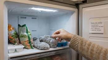 Primer plano de una mano introduciendo calcetines escarchados y planos en un congelador lleno de hielo y bolsas de verduras congeladas.