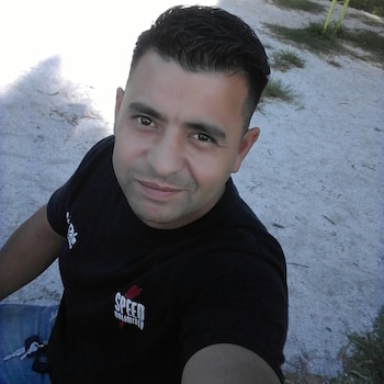 Primer plano de un hombre joven de tez morena y cabello oscuro, con corte degradado, vistiendo una camiseta negra con un logo blanco y rojo