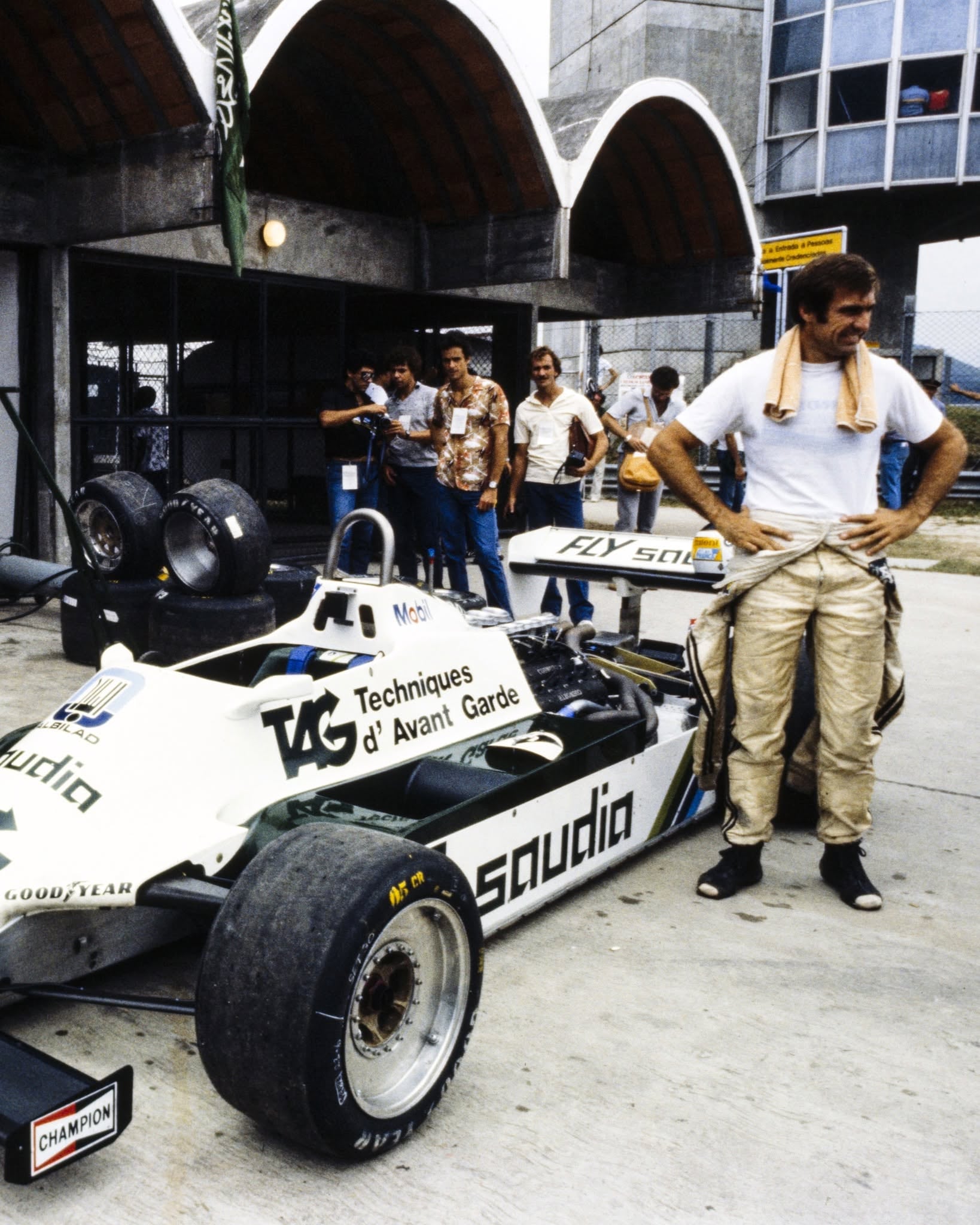 Carlos Reutemann, piloto de Fórmula 1, se muestra relajado junto a su monoplaza blanco con patrocinio Saudia en el área de boxes.