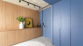 Interior moderno con pared de madera y armarios azules, techo de hormigón y luces de riel, un jarrón blanco, y un cuadro amarillo con un plátano negro.