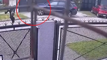 Toma desde detrás de una reja de metal que muestra una calle con dos automóviles y una figura señalada con un círculo rojo