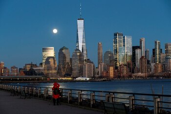 Una mujer intenta tomar una foto de la luna llena conocida como “Luna Fría” mientras se eleva detrás del One World Trade Center, vista desde Jersey City, Nueva Jersey, Estados Unidos, el 29 de diciembre de 2020. (REUTERS/Eduardo Muñoz)