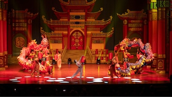 Escenario teatral con telón de fondo de arquitectura china, dos dragones rojos y azules siendo manipulados, acróbatas con vestuario tradicional y linternas