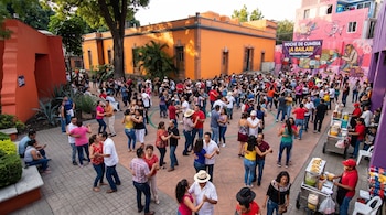 Decenas de parejas bailan en un patio al aire libre entre edificios coloridos, un cartel de evento y carritos de comida.