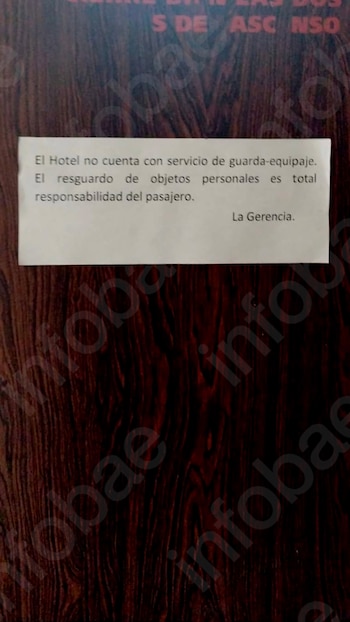 Primer plano de un cartel blanco pegado a una puerta de madera oscura, con texto en español sobre la responsabilidad del pasajero en el resguardo de equipaje