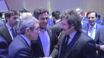 Javier Milei sonríe mientras conversa con varios hombres vestidos con traje formal durante un evento en interiores