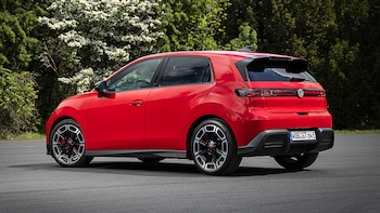 Vista trasera tres cuartos de un Volkswagen ID.Polo GTI rojo. El vehículo deportivo eléctrico está estacionado al aire libre con árboles y flores blancas de fondo