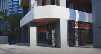 Fachada de un edificio moderno con la entrada de la farmacia Pharma&GO, letrero luminoso, ventanales, pavimento y árboles