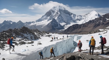 Grupo de montañistas con mochilas y cascos caminando sobre un glaciar y terreno rocoso, con grandes montañas cubiertas de nieve bajo un cielo azul claro.