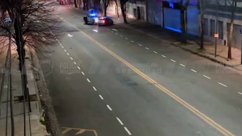 Vista desde arriba de una avenida nocturna con dos vehículos policiales detenidos en el centro de la calzada y aceras a los lados