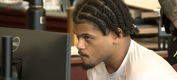 Primer plano del perfil derecho de un hombre joven con trenzas y barba incipiente, mirando hacia un monitor Dell negro a la izquierda