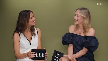 Dos mujeres sentadas sonriendo frente a frente. La mujer de la izquierda lleva un top blanco y negro. La de la derecha, un top azul. Ambas sujetan objetos con el logo ELLE. Fondo verde