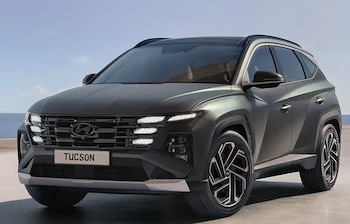 Un automóvil SUV Hyundai Tucson 2024 de color gris oscuro, visto de frente en un exterior con cielo azul y un cuerpo de agua al fondo