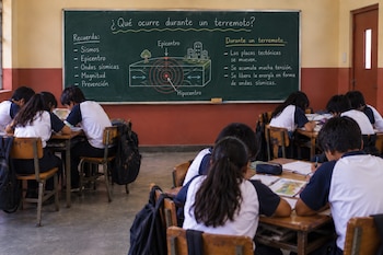 Estudiantes sentados en carpetas escolares frente a una pizarra verde con esquemas e información escrita sobre terremotos