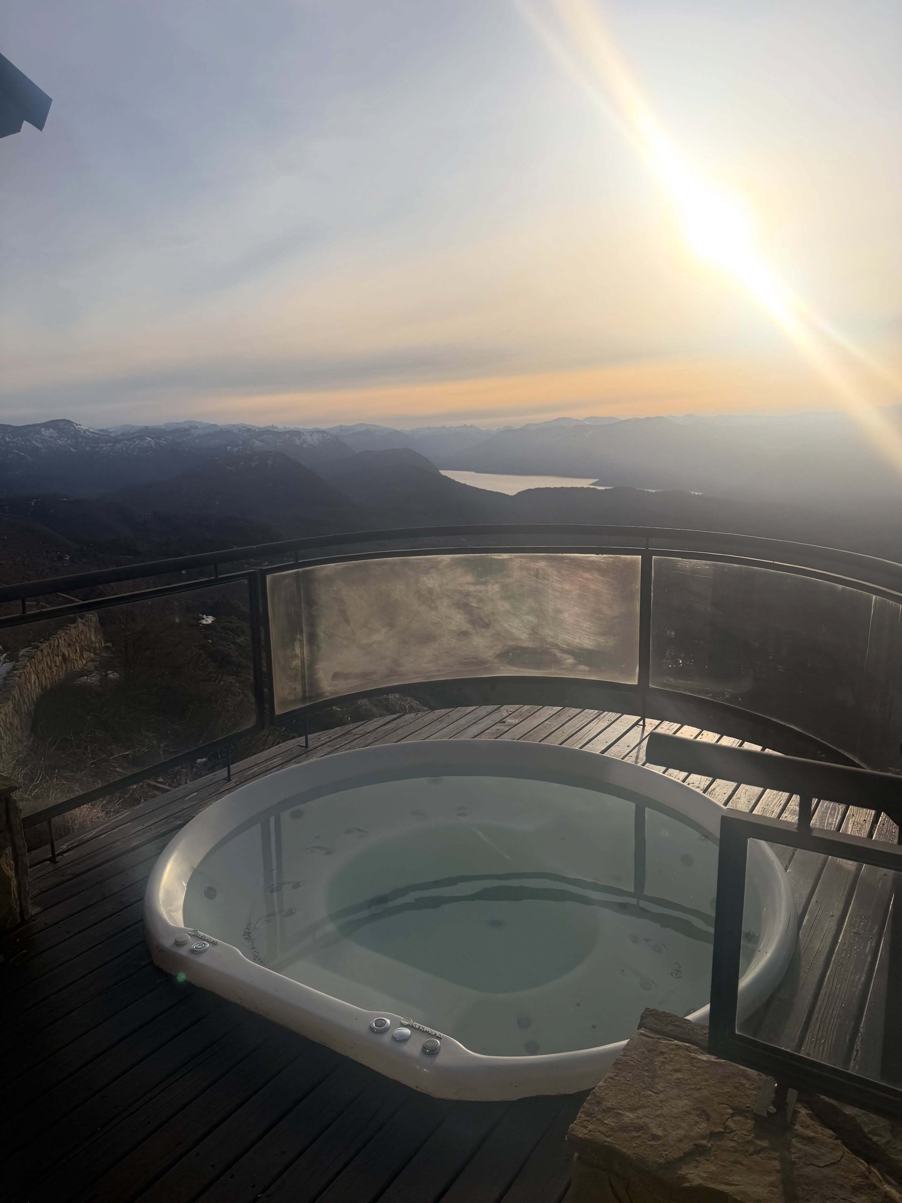 Un hidromasaje sobre un deck de madera ofrece una vista hacia las montañas y un lago
