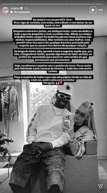 Vinícius Júnior, con gorra y gafas de sol, sonríe mientras una mujer rubia con gafas de sol se apoya en él, ambos posando para una selfie en blanco y negro