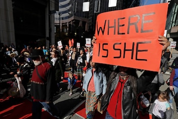 Personas marchan por la calle mientras sostienen un cartel rojo que dice WHERE IS SHE y otras pancartas