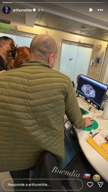 Un hombre calvo con chaqueta acolchada verde, visto de espaldas, mira una tomografía médica en la pantalla de una computadora en un entorno hospitalario
