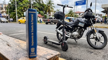 Un libro azul titulado Reglamento de Tránsito de Panamá sobre una banca de madera, con un monopatín eléctrico y una motocicleta detrás.