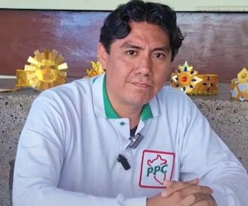 Un hombre con polo blanco con el logotipo del PPC mira a la cámara frente a una pared con adornos dorados