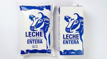 Primer plano de una bolsa de leche UHT de 900 ml y un cartón de 1 litro, ambos blancos con diseño de vaca de color azul y texto LECHE ENTERA.