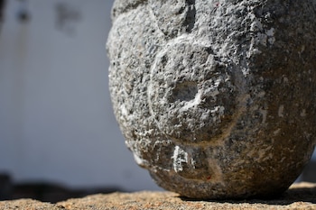 Primer plano de una escultura prehispánica de piedra basáltica gris, mostrando un ojo profundo y parte de una mejilla con textura rugosa