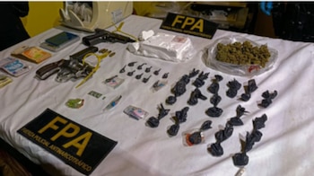 Armas de fuego, dinero en efectivo, envoltorios de sustancias y distintivos de la Fuerza Policial Antinarcotráfico sobre una mesa