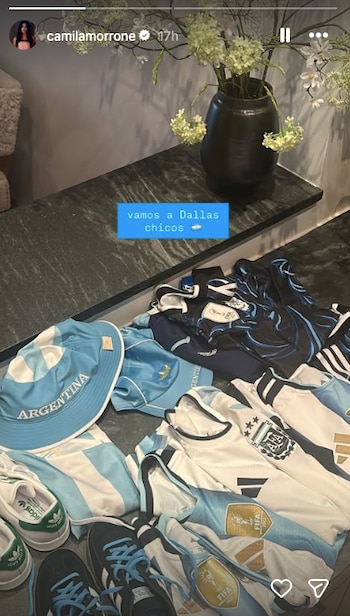 Múltiples camisetas, un sombrero y zapatillas de la selección argentina de fútbol sobre una superficie oscura, junto a un florero con flores
