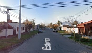 Vista de una calle residencial con viviendas, automóviles estacionados, postes de luz y la palabra Estomba inscrita en el asfalto