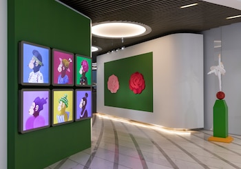 Una sala de exhibición de arte con seis pantallas iluminadas mostrando figuras de simios coloridas, dos rosas en una pared verde y una escultura de bailarina blanca
