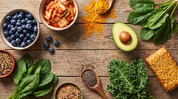 Arándanos, kimchi, cúrcuma, aguacate, espinacas, lentejas, semillas de chía, col rizada y tempeh dispuestos sobre una mesa de madera.