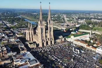 Vista aérea de una basílica de estilo neogótico con dos torres y una multitud congregada en la plaza situada frente al edificio