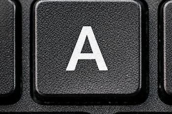 Primer plano de la tecla negra con la letra 'A' blanca de un teclado de computadora, mostrando la textura granulada de la superficie.