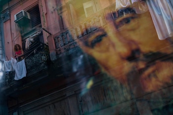 Una mujer cubana que tiende ropa en su balcón se refleja en una ventana decorada con un cartel del líder cubano Fidel Castro en La Habana Vieja, Cuba (AP Foto/Dado Galdieri/Archivo)