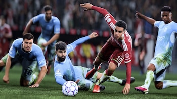 Cinco futbolistas en un campo de césped, tres con camiseta celeste y dos con camiseta roja, disputan un balón blanco y morado