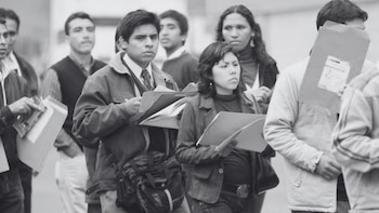 Varias personas hacen fila en la calle mientras sostienen carpetas de papel y documentos con sus manos