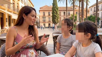 Karen Schwarz sentada en una terraza al aire libre, conversando con dos niñas con las caras pixeladas. Al fondo, edificios de estilo mediterráneo y palmeras.