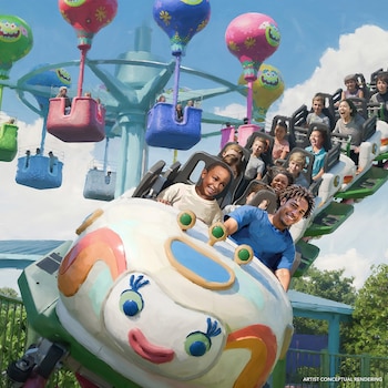 Personas de diversas edades sonríen mientras viajan en una colorida montaña rusa con un personaje sonriente en el frente, y globos aerostáticos de paseo al fondo