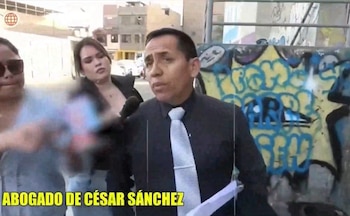 Un hombre con camisa oscura y corbata clara, una mujer con micrófono y otra persona. El fondo muestra un muro con grafitis, edificios y el texto "ABOGADO DE CÉSAR SÁNCHEZ"