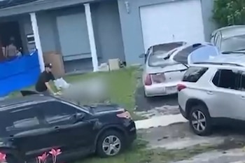 Fachada de una casa con vehículos estacionados, una persona en el jardín delantero y un área difuminada sobre el césped