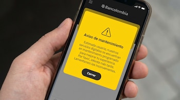 Primer plano de una mano sosteniendo un smartphone con la aplicación de Bancolombia abierta y un pop-up amarillo que indica 'Aviso de mantenimiento'.
