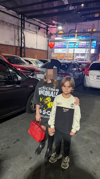 Dos niños posando en un estacionamiento por la noche; uno lleva gorra y camiseta oscura con estampado amarillo, el otro un buzo bicolor blanco y negro