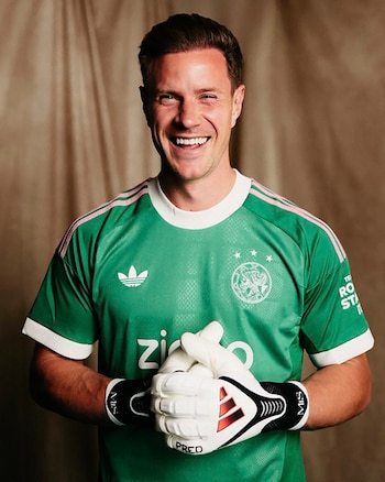 Hombre sonriendo con camiseta de portero verde y guantes blancos. En la camiseta se ven los logos de Adidas y del AFC Ajax