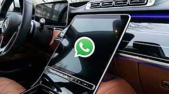 Primer plano de la pantalla de infoentretenimiento de un carro moderno con el logo de WhatsApp; se ven partes del volante, tablero y asientos de cuero.