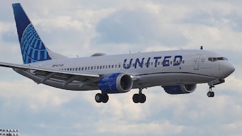 Un avión blanco de United Airlines con detalles azules y el tren de aterrizaje desplegado vuela bajo un cielo nublado