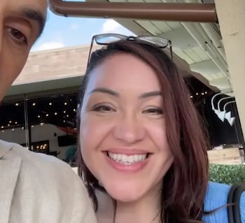 Primer plano de una mujer con cabello castaño rojizo y gafas en la cabeza sonriendo a la cámara; parte del rostro de un hombre es visible a la izquierda