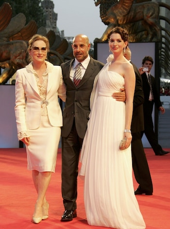 Meryl Streep, en traje blanco, y Anne Hathaway, en vestido blanco, posan junto a un hombre en un traje oscuro sobre una alfombra roja