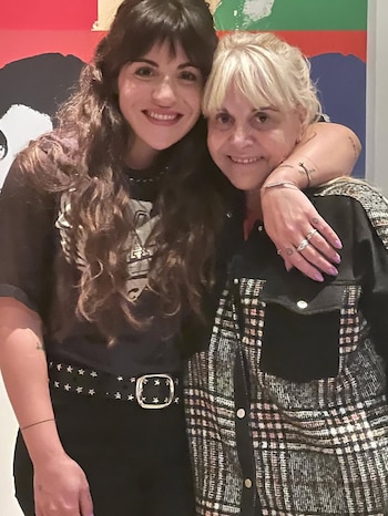 Claudia Villafañe, de cabello rubio, abraza a su hija Gianinna Maradona, de cabello oscuro y rizado, ambas sonriendo a cámara frente a un mural colorido