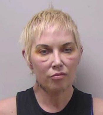 Primer plano de Kim Mathers con cabello rubio corto, moretones alrededor de los ojos y en el rostro, usando una camiseta oscura, en una ficha policial