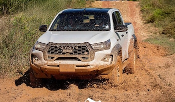 Camioneta pickup Toyota Hilux blanca cubierta de barro en un camino de tierra. Detrás se observa vegetación de color verde